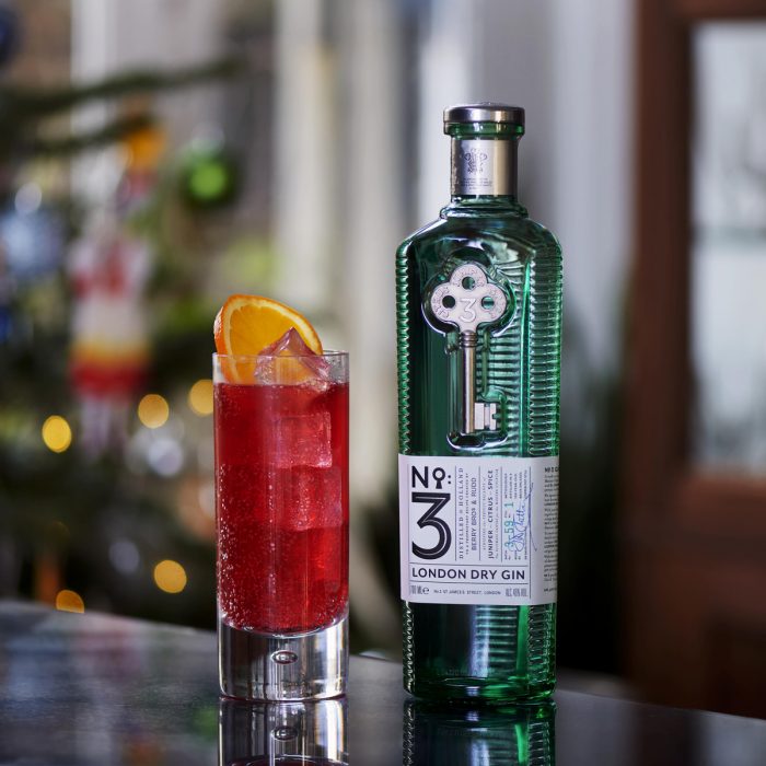 A bottle of No.3 Gin stands next to a scarlet cocktail in a highball glass