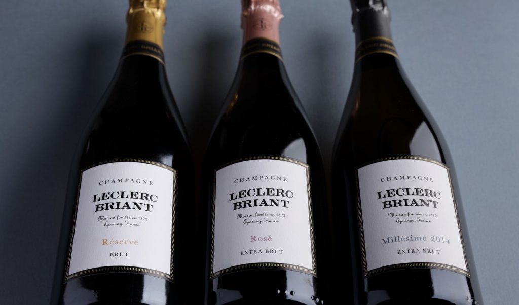 Three wines from Leclerc Briant - Reserve, Rose and 2014 Vintage lie on a dark grey background. They look sleek and elegant. 