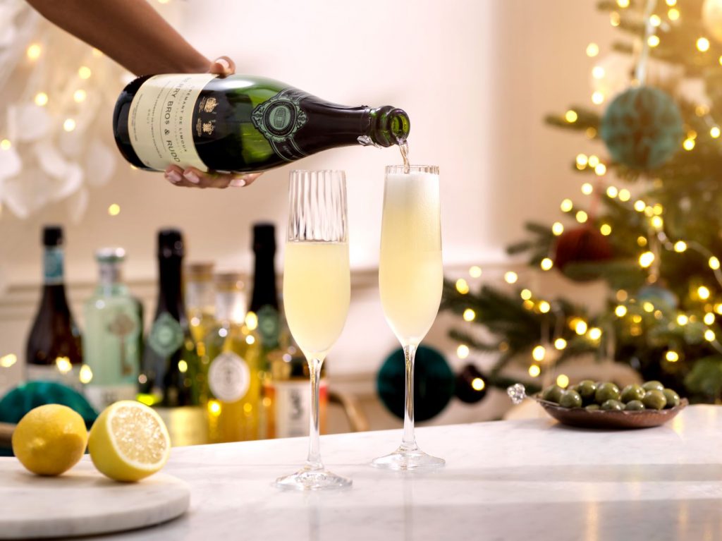 A bottle of sparkling wine is being poured into a Champagne flute to create a warming, ginger and gin cocktail