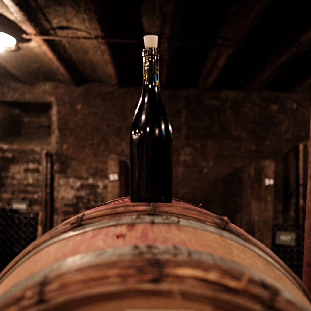 In the cellars of Burgundy, a bottle of wine - closed with a stopper - sits on top of a barrel.
