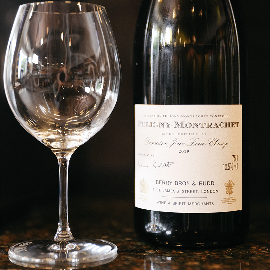 A close-up shot of the 2019 Own Selection Puligny-Montrachet beside an empty wine glass 