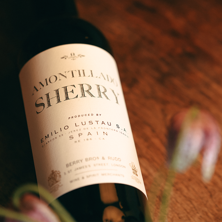 A bottle of Amontillado Sherry lies on a wooden table, behind the soft blur of pink-petalled flowers which just about edge into view.